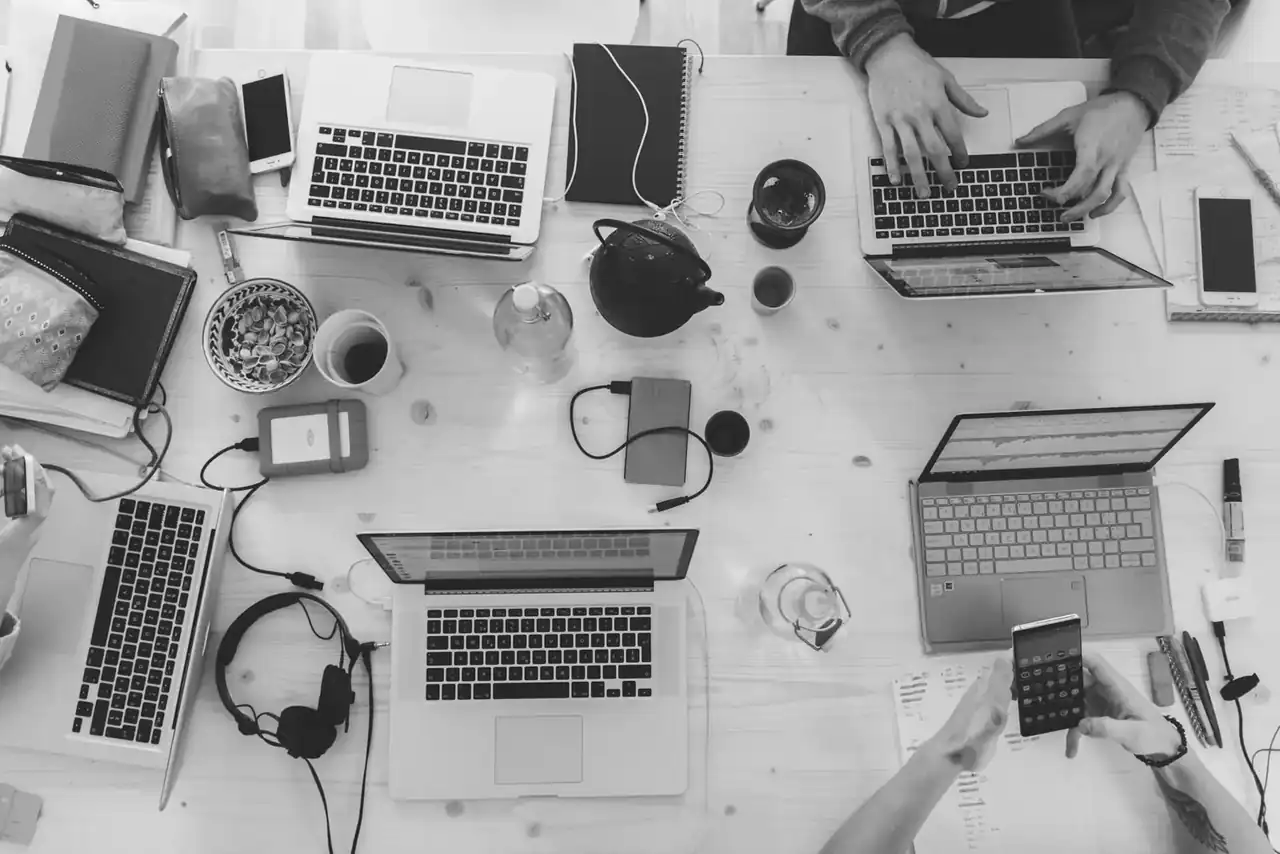 Laptops, notes and coffee on a shared work desk, seen from above
